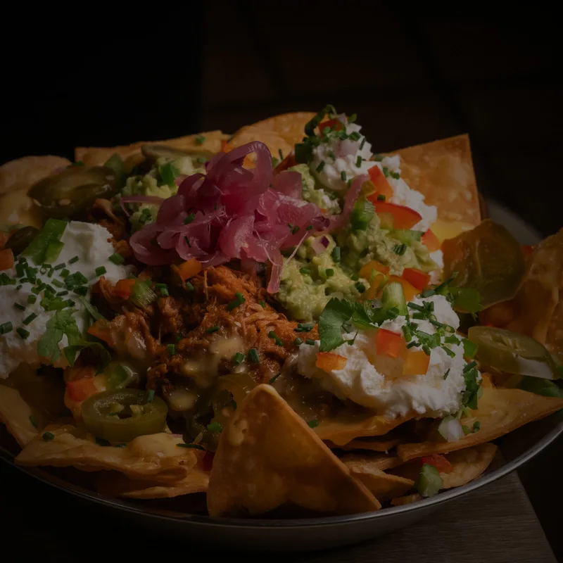 Nachos Caseros, Totopos de maíz caseros, chili con carne mechada, salsa de queso cheddar